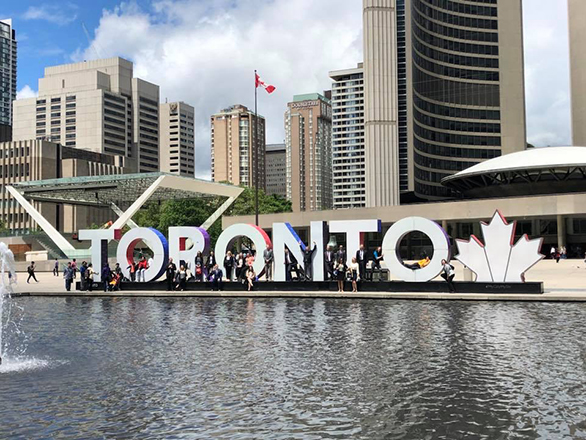 Photo of downtown Toronto with a group of students gathered at a Toronto sign.
