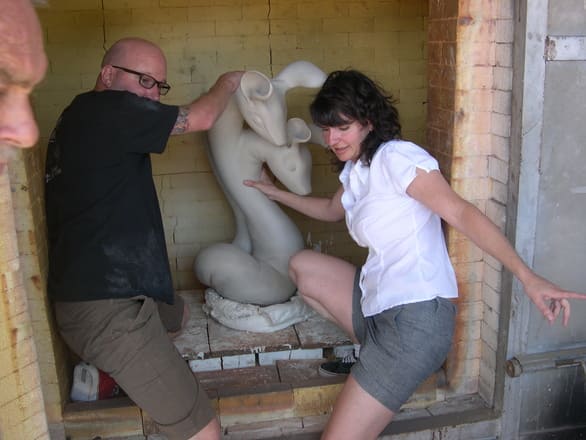 Art professor Rebecca Bogard placing large ceramic piece into a kiln with a helper.