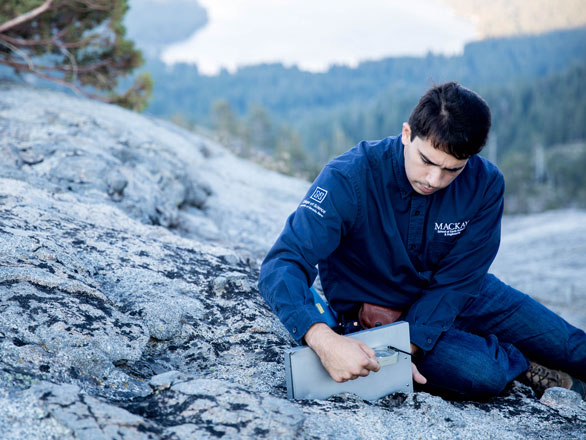 Student measuring strike and dip of a joint plain in granite rock.