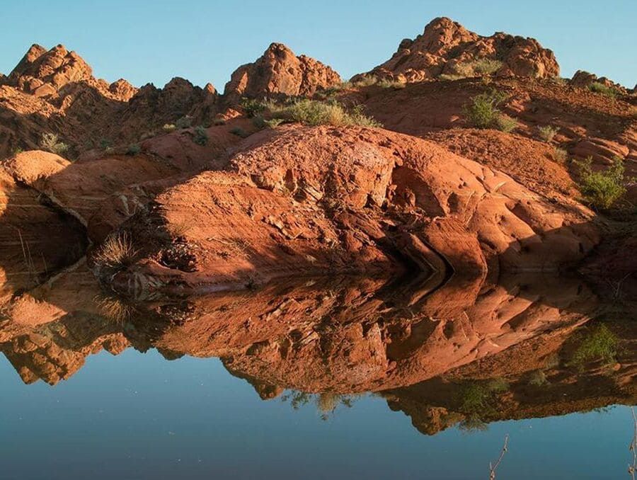 Red sandstone rocks overlook a small blue lake with its reflection.