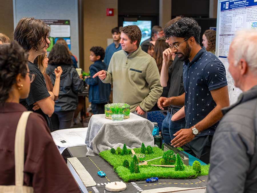 Students and attendees gather around a display featuring a model landscape with roads and greenery.