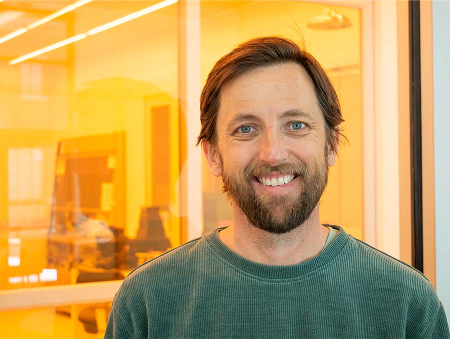 Russ Renzas standing in front of a window looking into a lab that has yellow lighting.