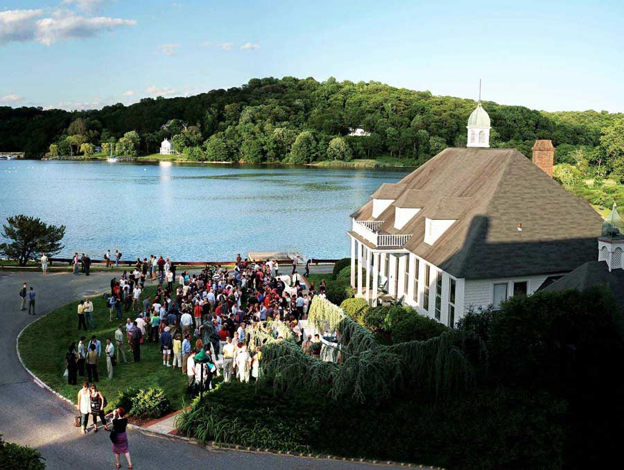 A drone photo of an old house on a bay with a large group of people on the lawn in front of the house.